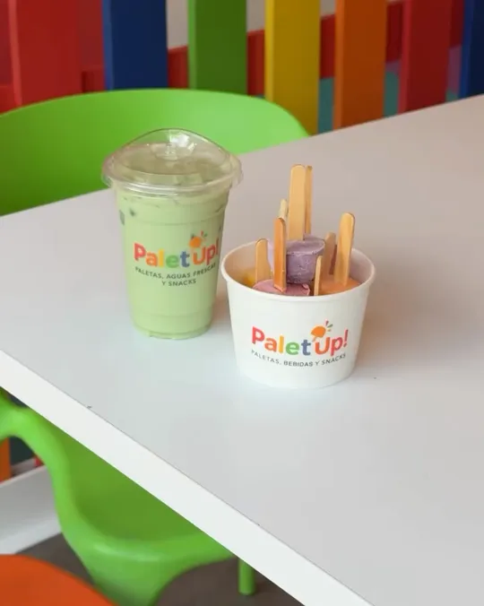Matcha y un bowl de paletas sobre una mesa blanca, con la cerca de colores de la tienda al fondo